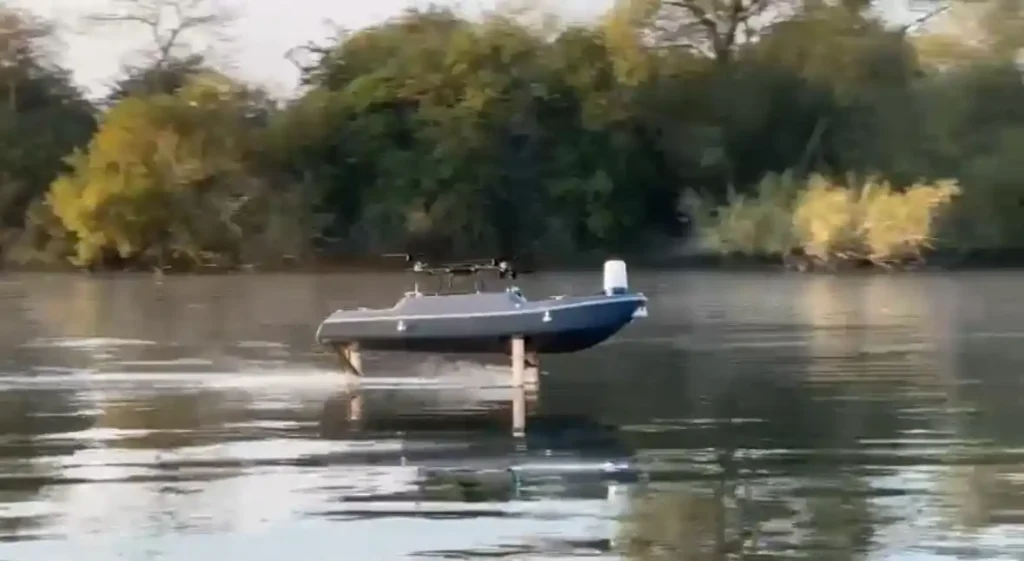 SeaGlide autonomous hydrofoil vessel gliding above the water during low-wake trials near a wooded shoreline